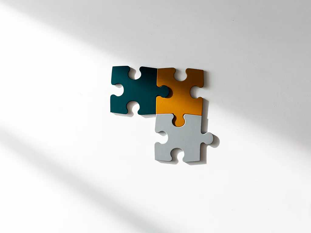 Drie onderling verbonden puzzelstukken in tinten blauwgroen, amber en leisteen op een wit bureau, bovenaanzicht.