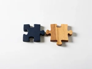 Standaard puzzelstuk naast handgesneden houten stuk op wit oppervlak, perfect passend bij een unieke vorm, minimalistische compositie.