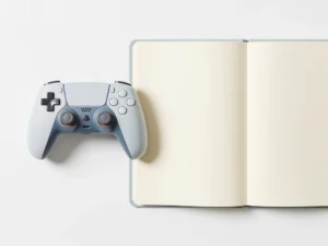 Gamecontroller en opengeslagen studieboek naast elkaar op wit oppervlak, strak bovenaanzicht in leisteenblauw en ivoorwit.