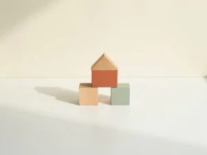 Houten speelblokken in terracotta en saliegroen op een wit bureau, met één uitvergroot blok als middelpunt.
