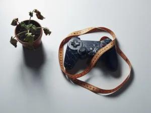 Gebarsten gamecontroller verstrengeld in meetlint naast verwelkte plant op wit bureau, minimalistische bovenaanzicht compositie.