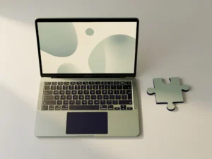 Open laptop met minimalistisch scherm op wit bureau, geometrisch puzzelstuk ernaast, salie groen en marineblauw kleurenpalet, bovenaanzicht.