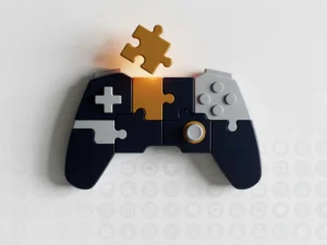 Geometrische gamecontroller van puzzelstukken op wit oppervlak, met een gloeiend amber stuk boven leerobjectivenpictogrammen in navy, amber en grijs.
